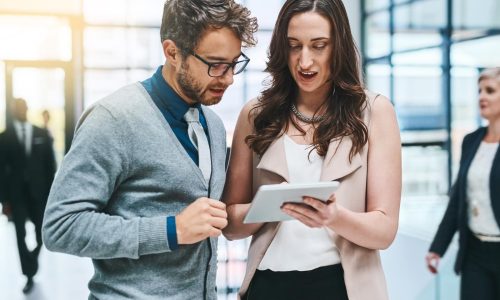 Cropped shot of two young businesspeople working on a digital tablet in a busy office.